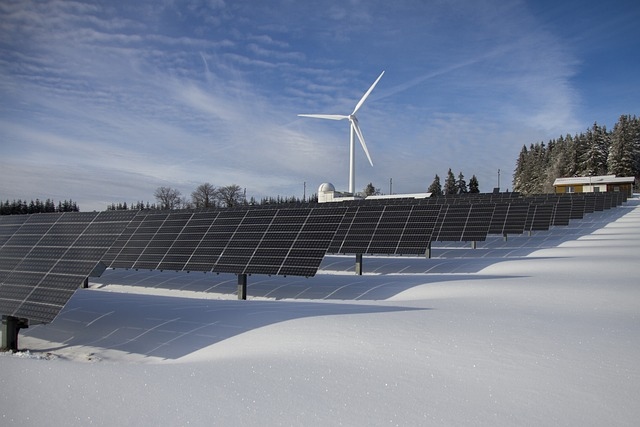 Solarpanele im Schnee, dahinter ein Windrad